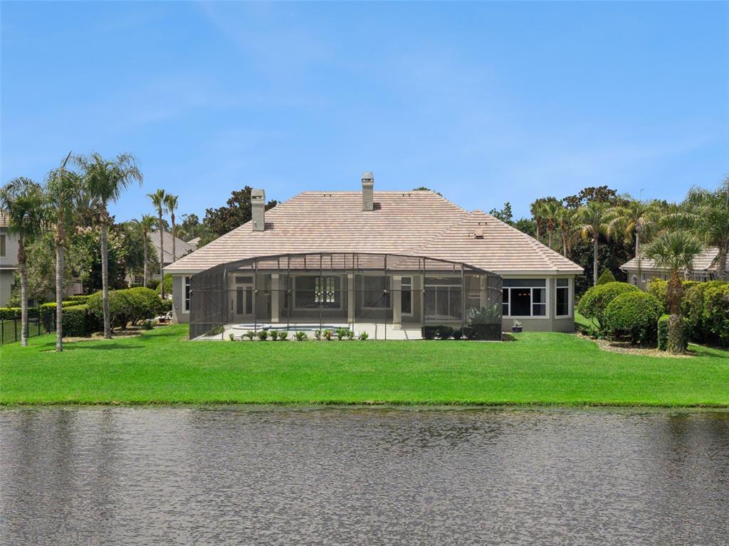 A rear exterior view of a house with a screened-in pool and a lakefront lawn — 4013 BERMUDA GROVE PLACE, LONGWOOD, FL