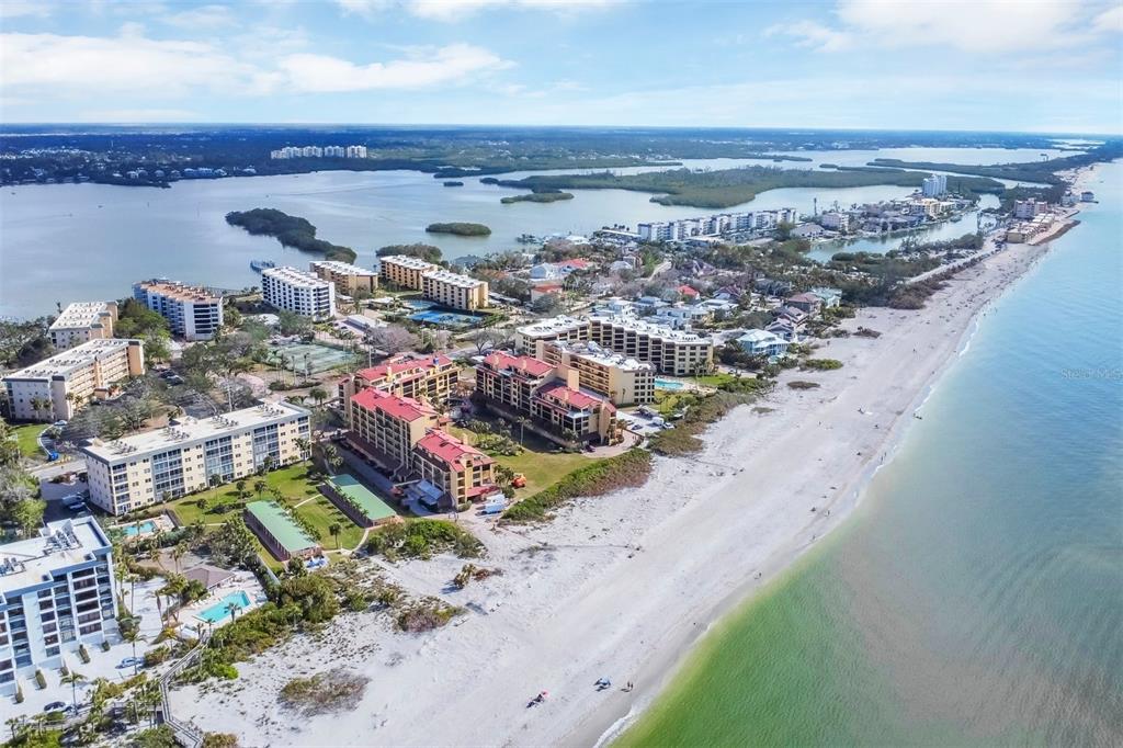 An aerial view shows multiple beachfront condominium buildings situated along a sandy coastline — 8625 MIDNIGHT PASS ROAD UNIT 506B, SARASOTA, FL