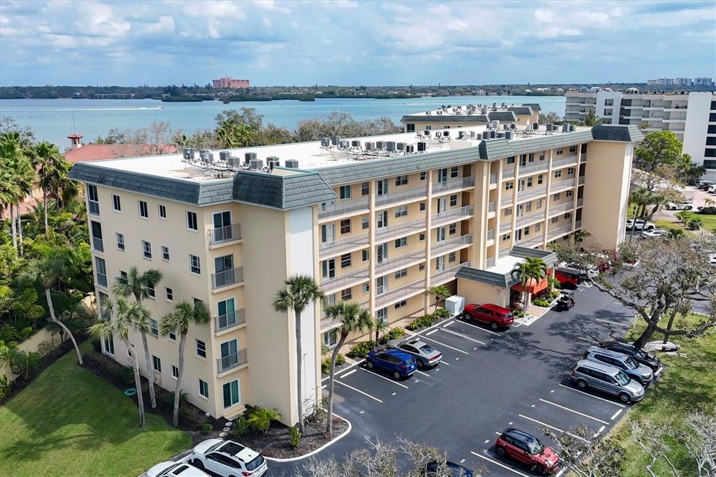 An aerial view shows a multi-story apartment building with a parking lot and waterfront background — 8625 MIDNIGHT PASS ROAD UNIT 506B, SARASOTA, FL
