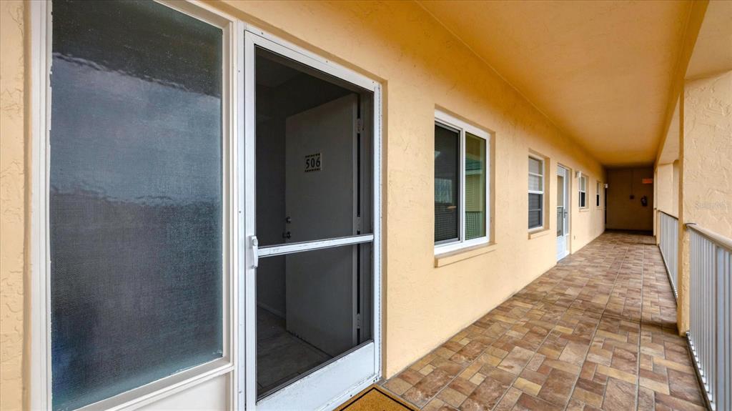 An exterior walkway features tiled flooring, a screen door to unit 506, and windows — 8625 MIDNIGHT PASS ROAD UNIT 506B, SARASOTA, FL