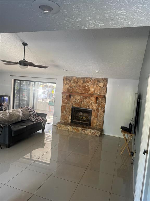 A living room features large light-colored floor tiles, a stone fireplace, and a ceiling fan — 2376 WINDSOR OAKS AVENUE, LUTZ, FL