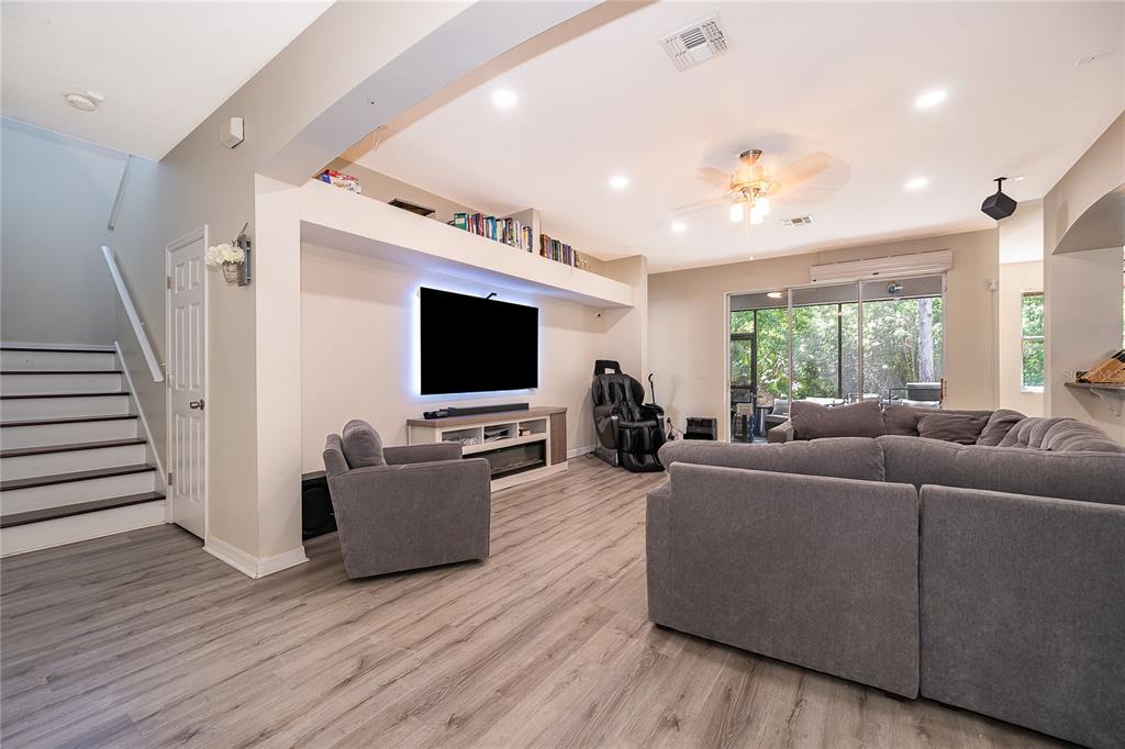 A living room features a wall-mounted television, gray sectional sofa, and stairs with wood treads — 9808 BENNINGTON CHASE DRIVE, ORLANDO, FL