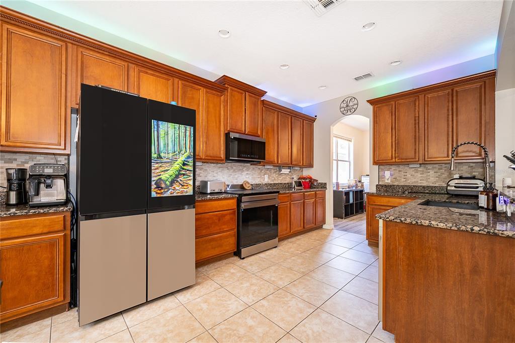A kitchen features wood cabinets, granite countertops, stainless steel appliances, and a smart refrigerator — 9808 BENNINGTON CHASE DRIVE, ORLANDO, FL