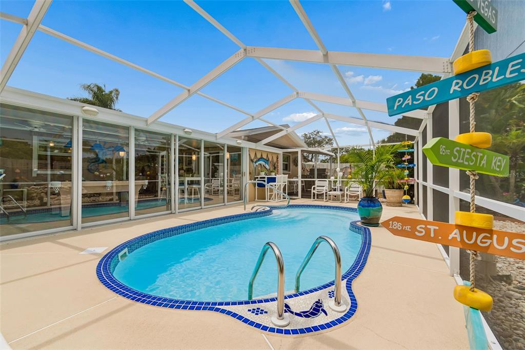 A screened-in patio features a kidney-shaped swimming pool and a decorative wooden signpost — 5843 APPLETREE ROAD, HOLIDAY, FL