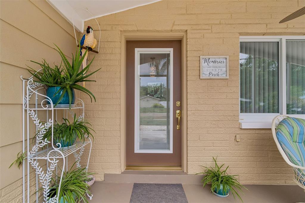 A front porch features a brown door, a white plant stand, and a decorative wall sign — 5843 APPLETREE ROAD, HOLIDAY, FL