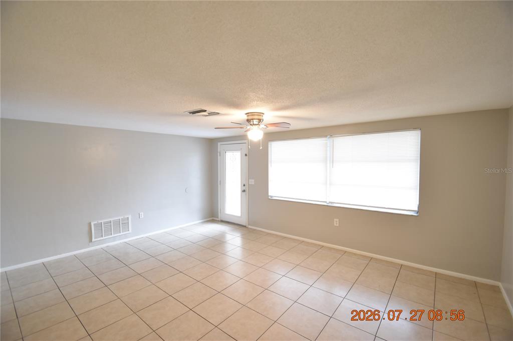 A living room features light-colored tile flooring, neutral walls, a ceiling fan, and large windows — 3221 TOPP DRIVE, HOLIDAY, FL