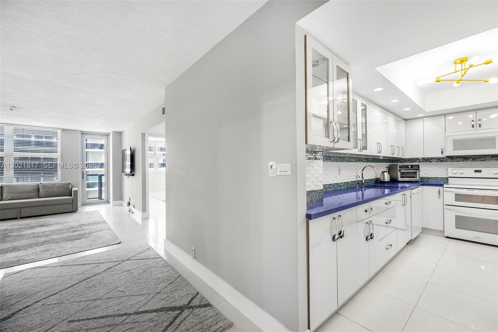 A kitchen with white cabinets and blue countertops sits adjacent to a living room — 9511 Collins Ave # 1202, Surfside FL 33154, SURFSIDE, FL