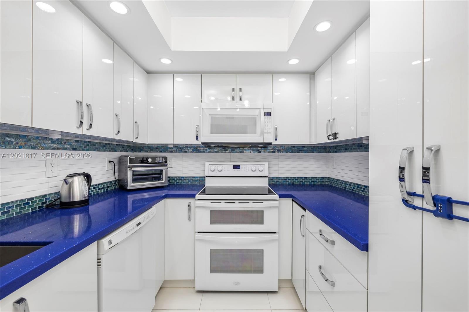 A kitchen features white cabinetry, blue countertops, a white stove, and a mosaic tile backsplash — 9511 Collins Ave # 1202, Surfside FL 33154, SURFSIDE, FL