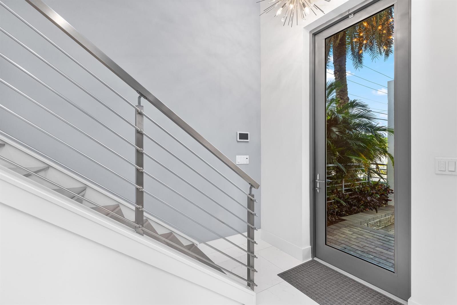A modern entryway features a glass door, white tile floors, and a metal stair railing — 1851 NW 40th Drive, Boca Raton FL 33431, BOCA RATON, FL