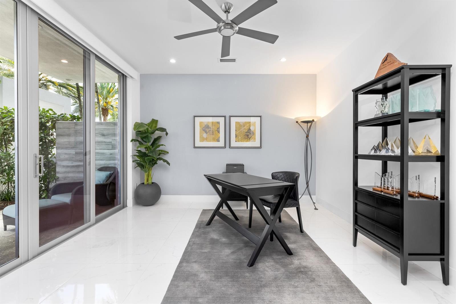 A modern home office features a black desk, shelving unit, and sliding glass doors to a patio — 1851 NW 40th Drive, Boca Raton FL 33431, BOCA RATON, FL