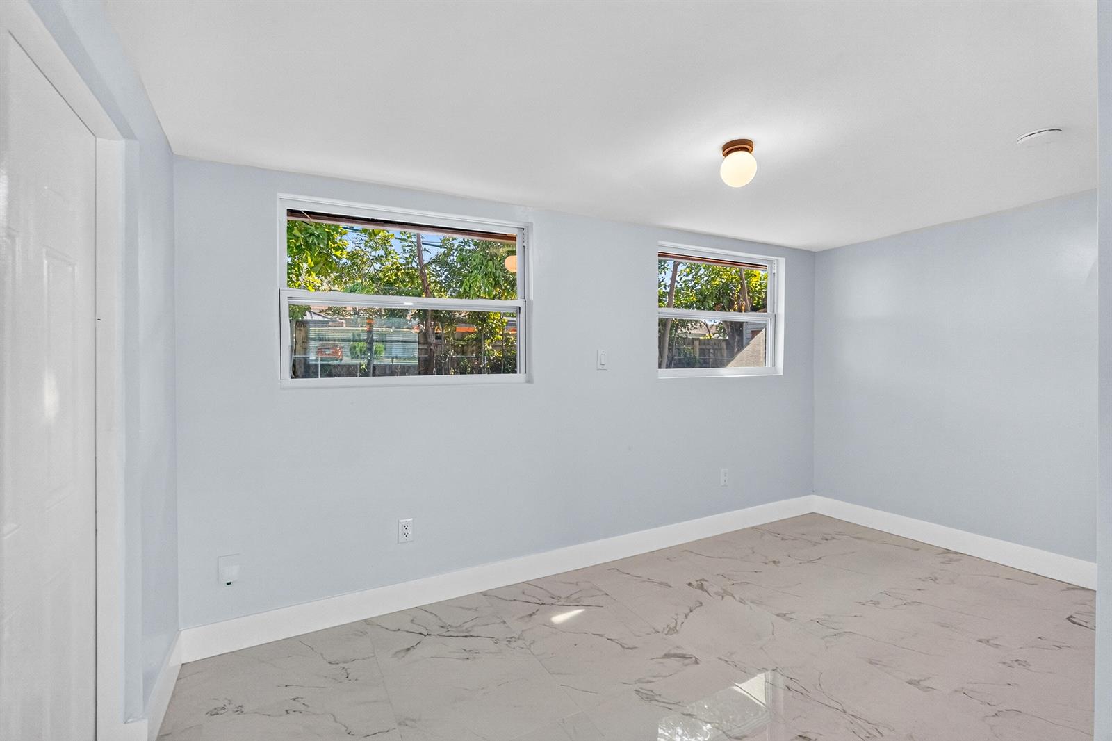 An empty room with light blue walls, white trim, and light-colored marble-patterned tile flooring — 1531 NE 33rd Street, Pompano Beach FL 33064, POMPANO BEACH, FL