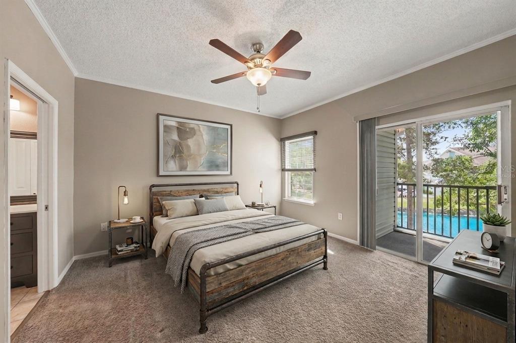 A bedroom with a rustic metal bed frame, ceiling fan, and a balcony overlooking water — 8350 SAVANNAH TRACE CIRCLE UNIT 106, TAMPA, FL