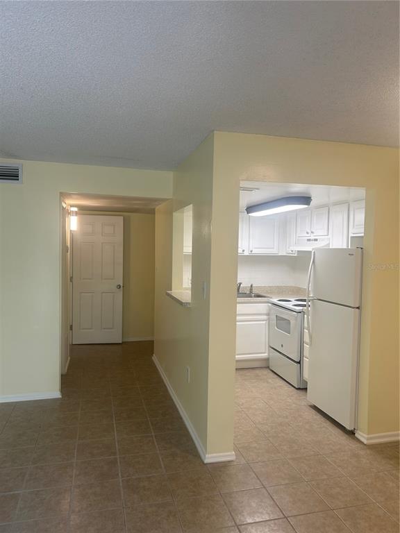 A kitchen with white cabinets and appliances is visible from a tiled living area — 2513 N ALAFAYA TRAIL UNIT 21, ORLANDO, FL