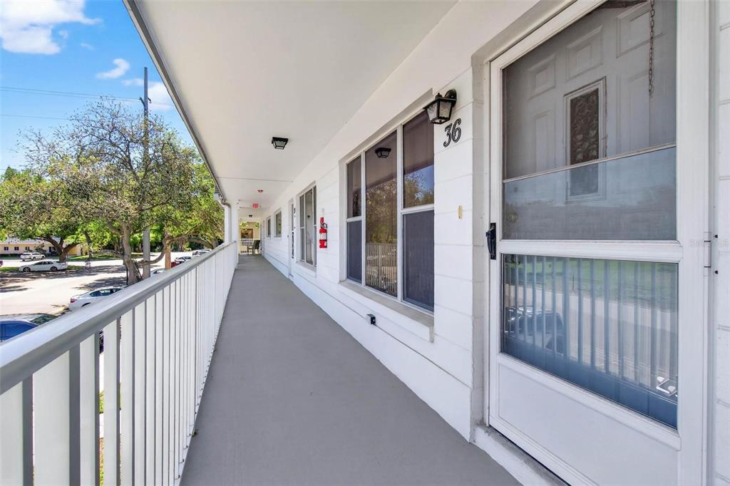 An exterior walkway with a white railing overlooks a parking lot beside a building entrance — 2220 SWEDISH DRIVE UNIT 36, CLEARWATER, FL