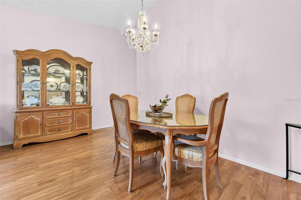 A dining room features a glass-topped table, cane-back chairs, a wooden hutch, and chandelier — 2220 SWEDISH DRIVE UNIT 36, CLEARWATER, FL
