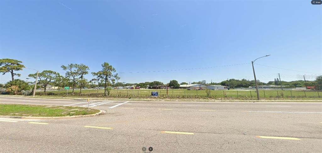 A wide, grassy vacant lot sits behind a chain-link fence along a paved road — HWY 60 E, LAKE WALES, FL