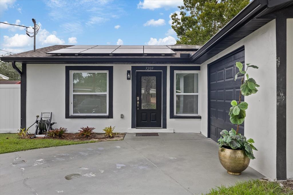 A single-story house exterior features white stucco walls, black trim, solar panels, and a driveway — 3209 E HANNA AVENUE, TAMPA, FL