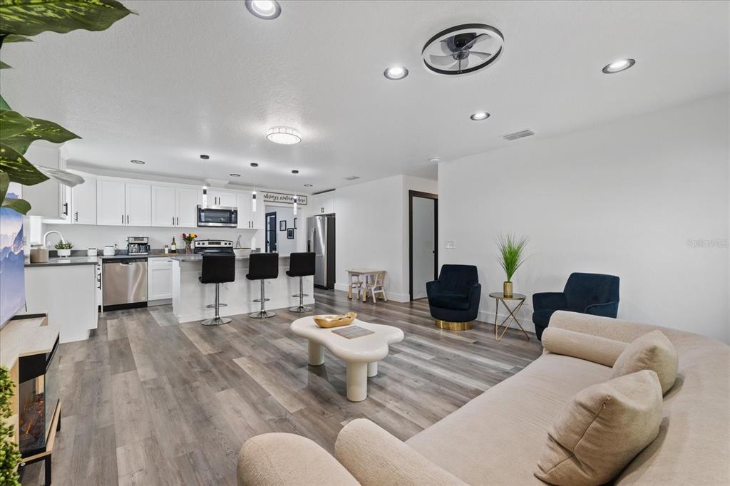 An open-concept living room and kitchen featuring white cabinetry, a breakfast bar, and wood flooring — 3209 E HANNA AVENUE, TAMPA, FL