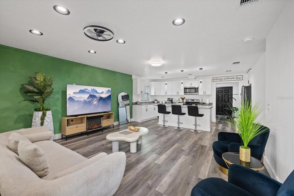 An open-concept living room and kitchen featuring a green accent wall, white cabinetry, and flooring — 3209 E HANNA AVENUE, TAMPA, FL