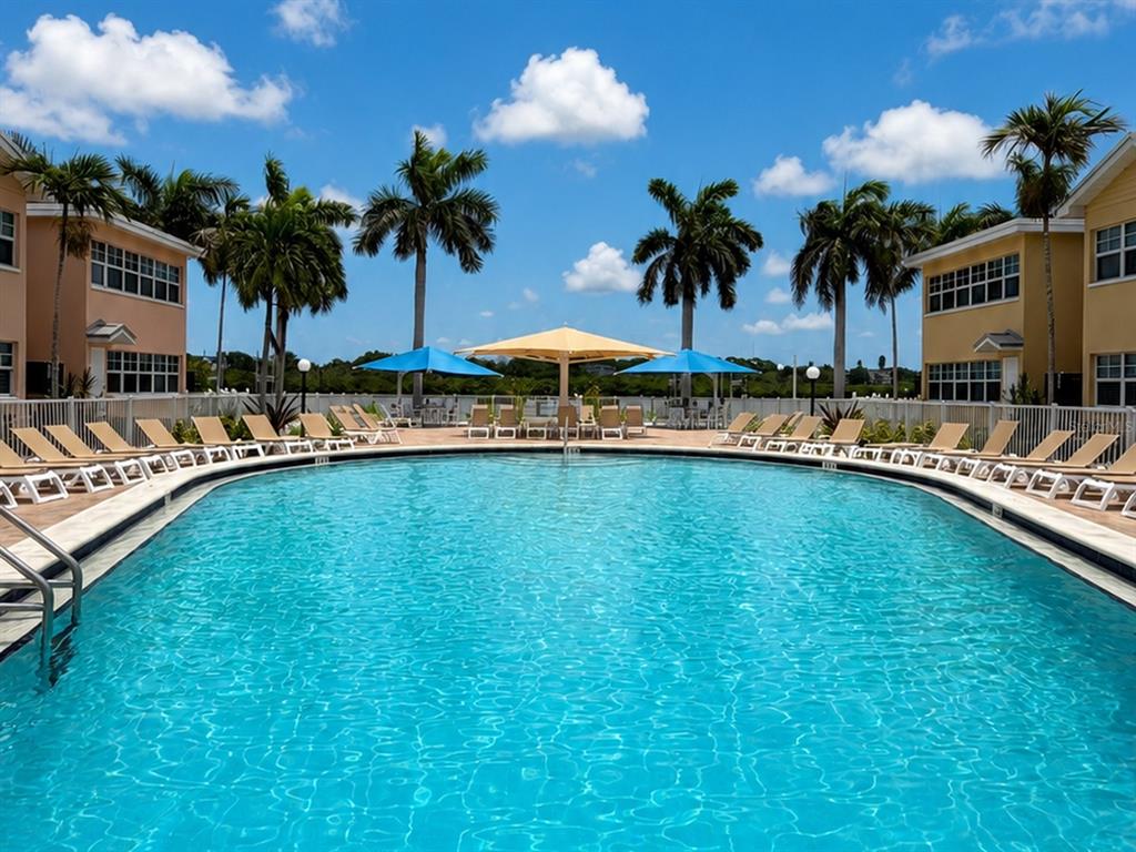 A swimming pool is surrounded by lounge chairs, palm trees, and two multi-story buildings — 19417 GULF BOULEVARD UNIT C106, INDIAN ROCKS BEACH, FL