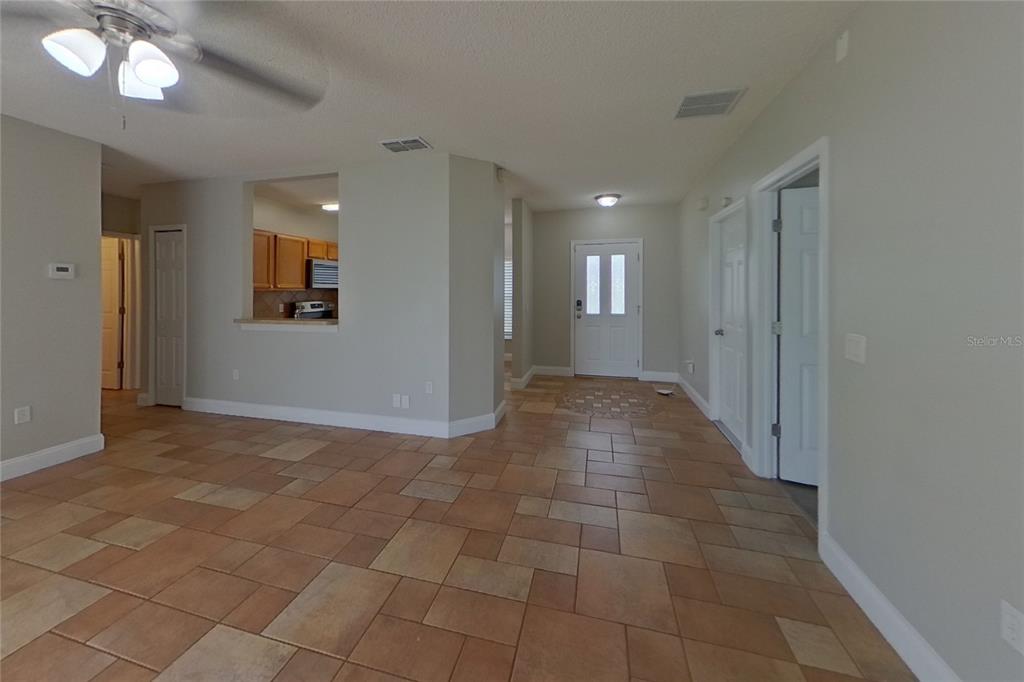 An interior view showing a tiled living area, an entryway, and a kitchen pass-through window — 1141 DONCASTER COURT, KISSIMMEE, FL