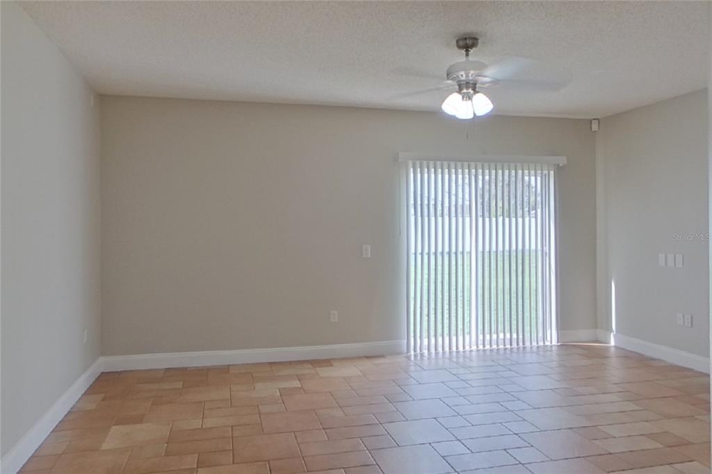 An empty room with tan tile flooring, light-colored walls, a ceiling fan, and sliding doors — 1141 DONCASTER COURT, KISSIMMEE, FL