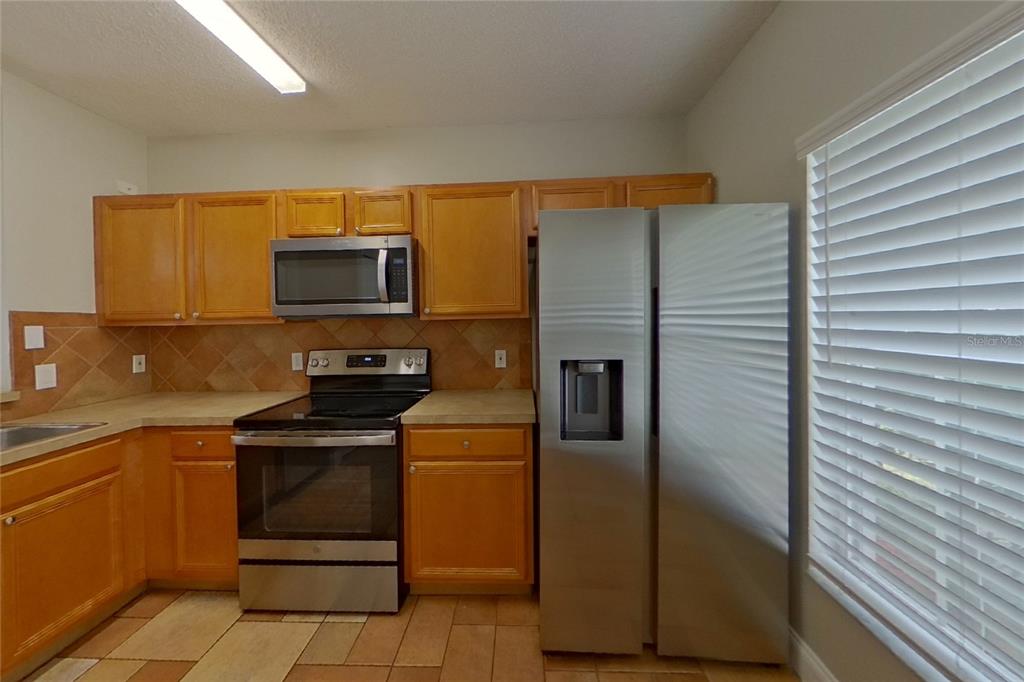 A kitchen features wood cabinets, stainless steel appliances, tile backsplash, and tile flooring — 1141 DONCASTER COURT, KISSIMMEE, FL