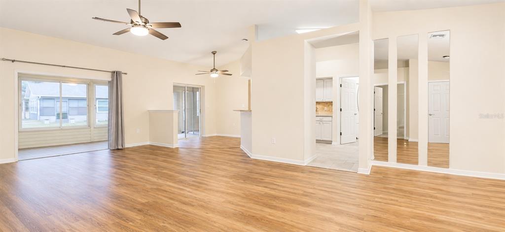 An open-concept living area features wood-look flooring, ceiling fans, and a mirrored wall section — 6032 MAGPIE DRIVE, LAKELAND, FL