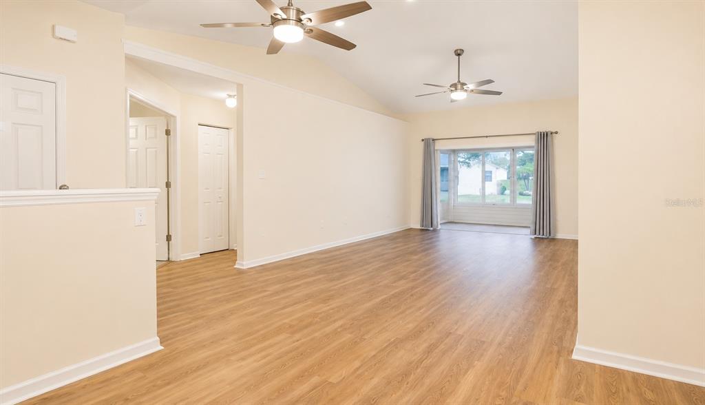 A spacious living room features light-colored walls, wood-look flooring, two ceiling fans, and large windows — 6032 MAGPIE DRIVE, LAKELAND, FL