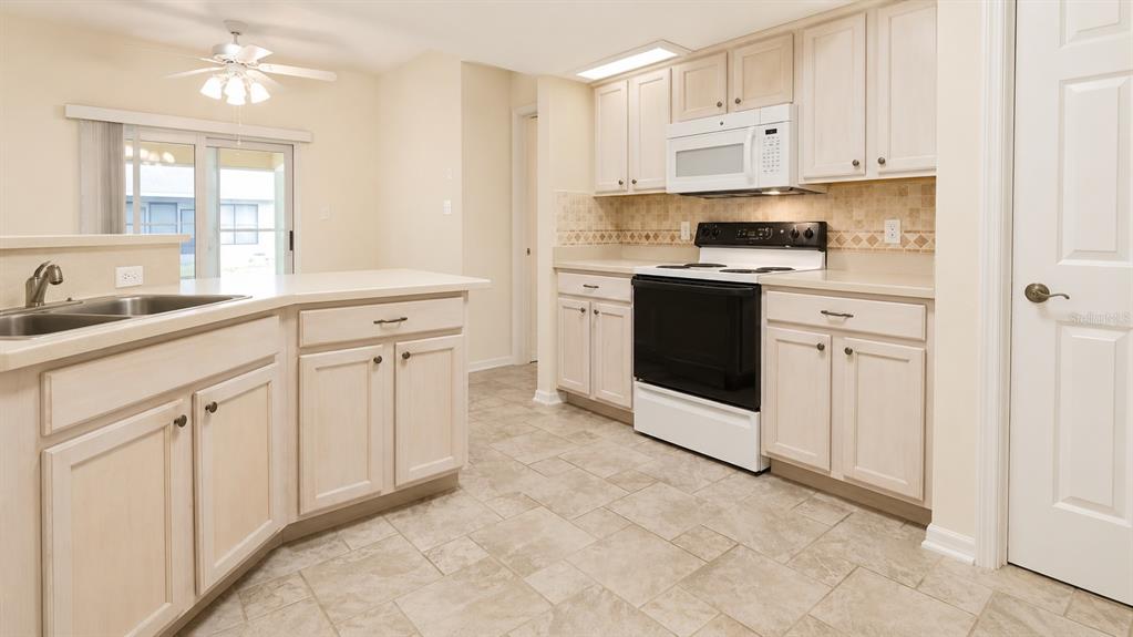 A kitchen with light-colored cabinets, tile flooring, a black stove, and a sliding glass door — 6032 MAGPIE DRIVE, LAKELAND, FL