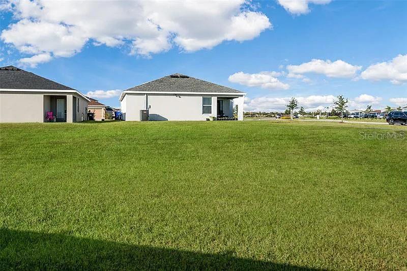 The rear exterior of two suburban houses overlooks a large, open grassy lawn — 3902 WHITE IBIS ROAD, LAKELAND, FL