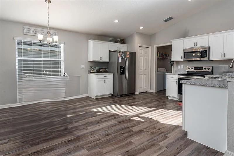 A kitchen and dining area feature white cabinets, stainless steel appliances, and wood-look flooring — 3902 WHITE IBIS ROAD, LAKELAND, FL