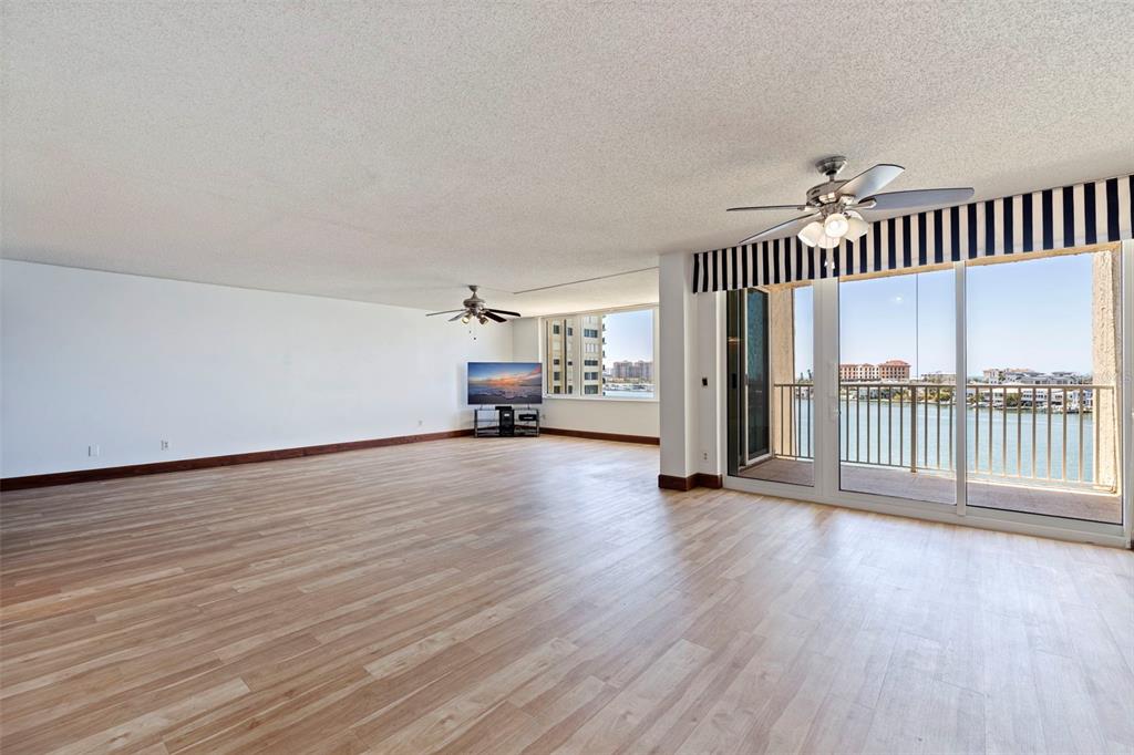 A spacious living room features light wood flooring, two ceiling fans, and a balcony view — 736 ISLAND WAY UNIT 504, CLEARWATER BEACH, FL