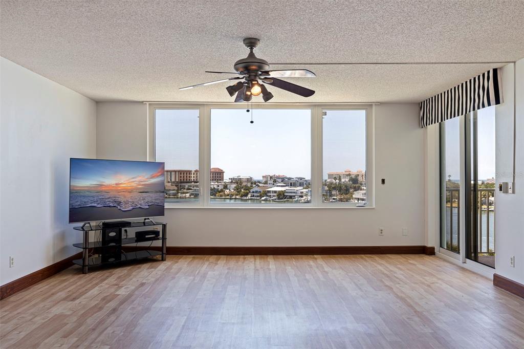 A living room with light wood flooring, a ceiling fan, and large windows overlooking water — 736 ISLAND WAY UNIT 504, CLEARWATER BEACH, FL