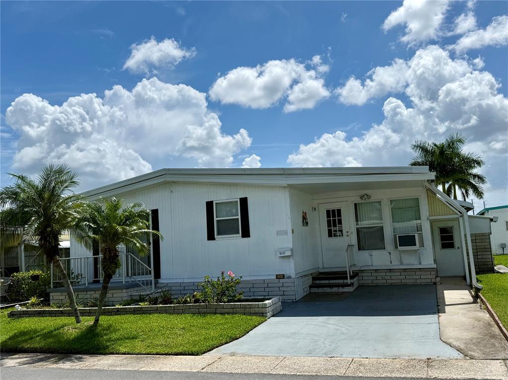 A single-story mobile home with white siding, a driveway, and palm trees under a cloudy sky — 82167 D STREET N UNIT 167, PINELLAS PARK, FL