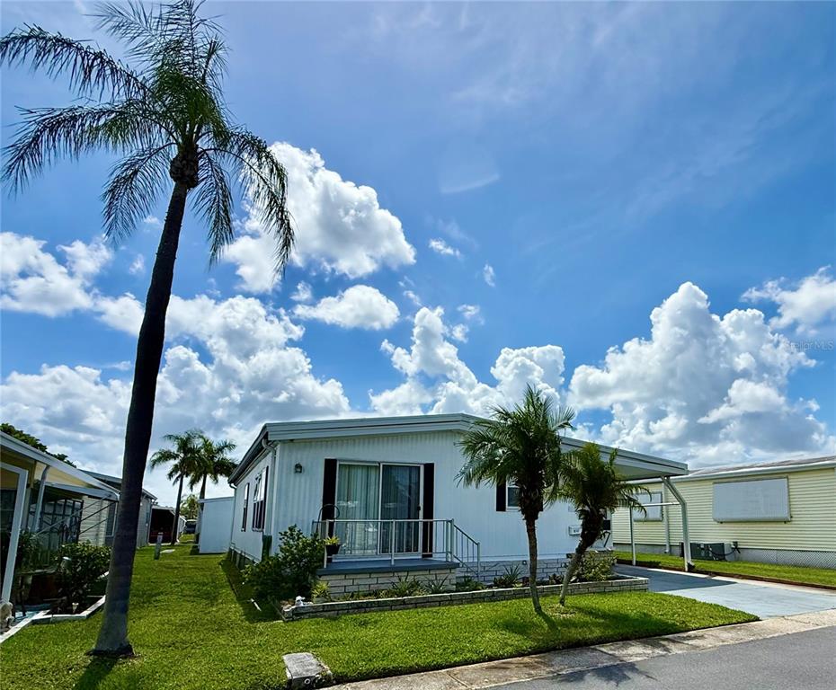 A white mobile home with a carport and palm trees under a cloudy blue sky — 82167 D STREET N UNIT 167, PINELLAS PARK, FL