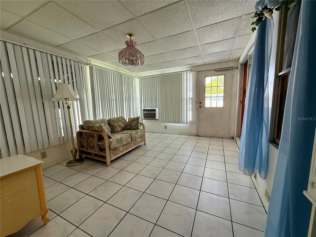A sunroom features white tiled flooring, a floral sofa, vertical blinds, and a ceiling light — 82167 D STREET N UNIT 167, PINELLAS PARK, FL