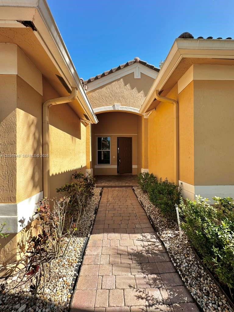 A paved walkway leads to the front entrance of a house with yellow stucco walls — 1831 Mariners Ln, Weston FL 33327, WESTON, FL