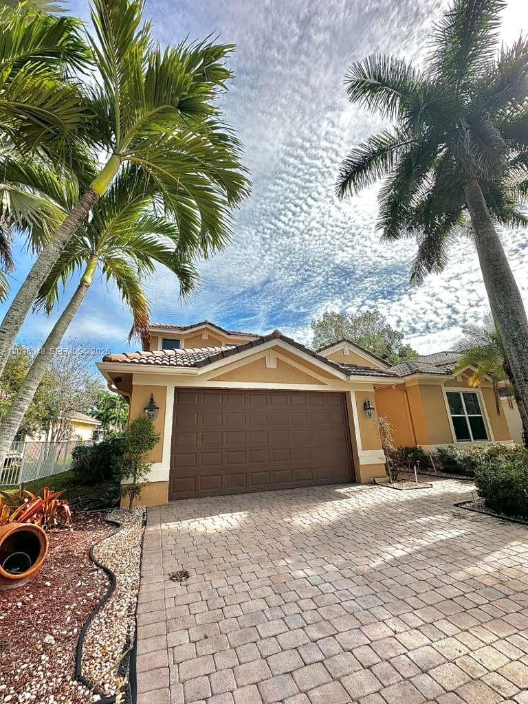 A tan house with a brown garage door and a paved driveway under palm trees — 1831 Mariners Ln, Weston FL 33327, WESTON, FL