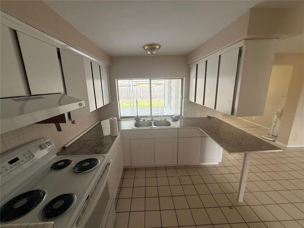 A kitchen features white cabinets, a laminate countertop, a white electric stove, and tile flooring — 3524 BRADFORD DRIVE, HOLIDAY, FL