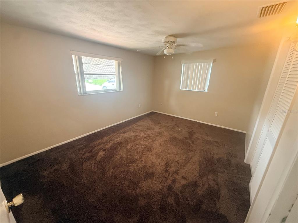 An empty bedroom with brown carpet, beige walls, a ceiling fan, and two windows — 3524 BRADFORD DRIVE, HOLIDAY, FL