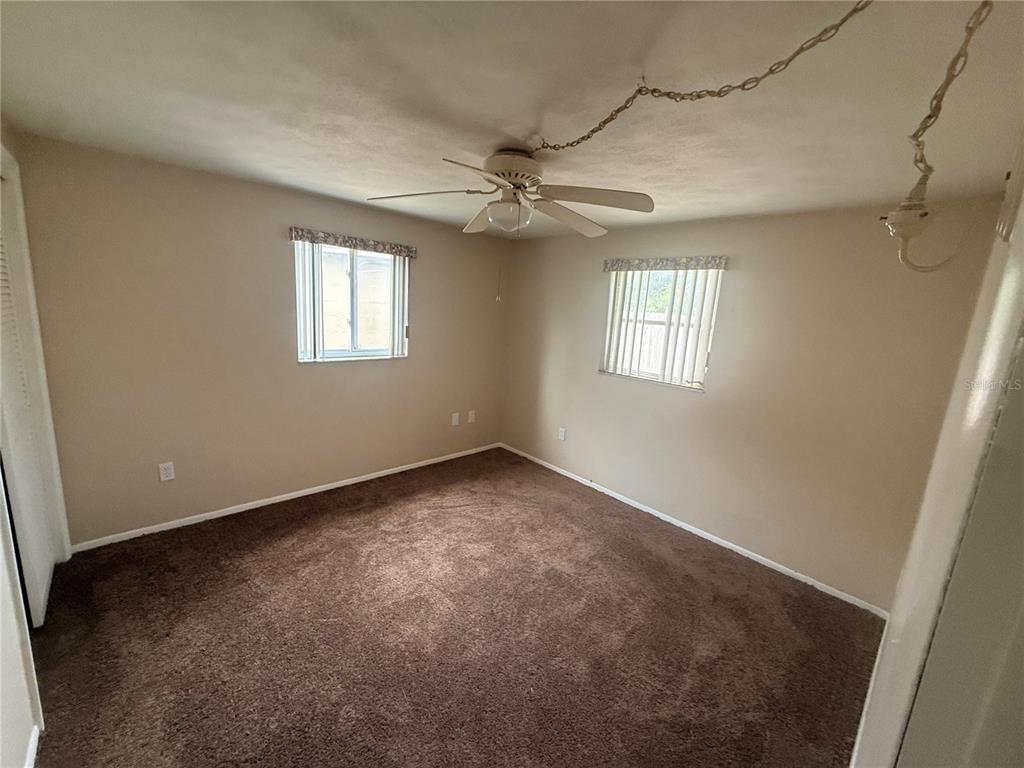 An empty bedroom features brown carpet, beige walls, two windows, and a ceiling fan — 3524 BRADFORD DRIVE, HOLIDAY, FL