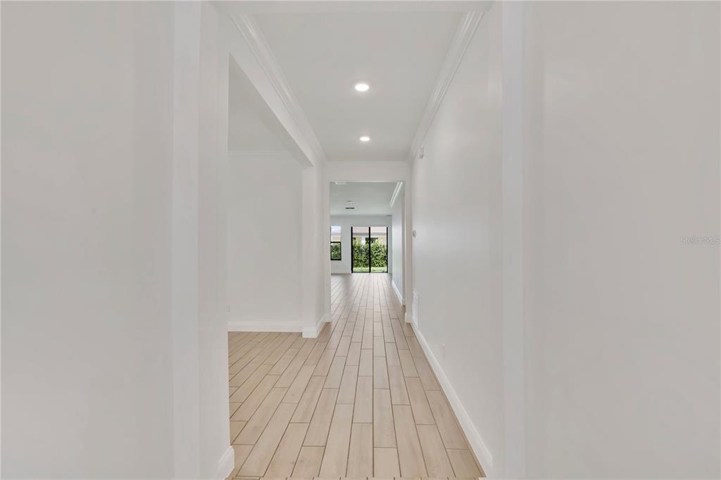 A hallway with light wood-look tile flooring leads toward a glass door and backyard view — 8318 VIVARO ISLE WAY, WINDERMERE, FL