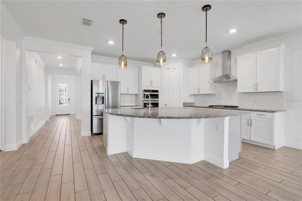 A modern kitchen features white cabinets, a curved granite island, and light wood-look tile flooring — 8318 VIVARO ISLE WAY, WINDERMERE, FL