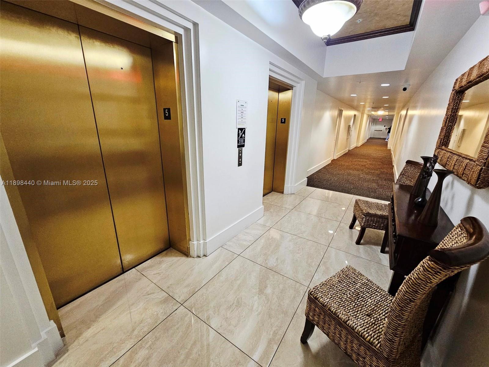 An elevator lobby features gold doors, tiled flooring, and a hallway with wicker chairs — 2280 SW 32nd Ave # 511, Miami FL 33145, MIAMI, FL