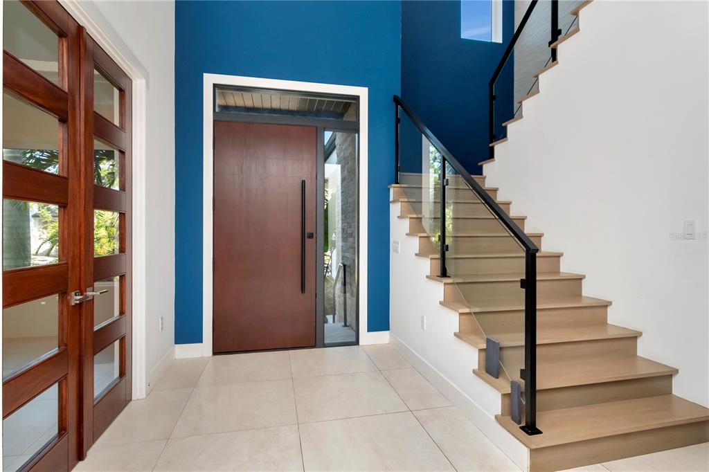 A modern entryway features a blue accent wall, a wooden front door, and a floating staircase — 4604 W LOWELL AVENUE, TAMPA, FL