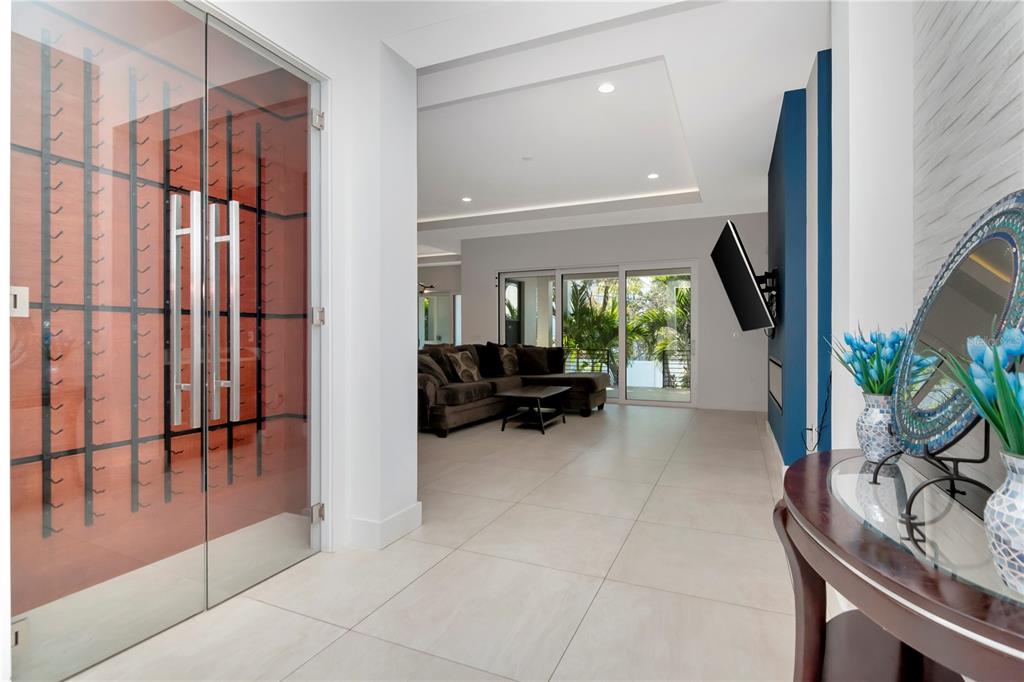 A glass-enclosed wine cellar sits beside a hallway leading to a living room with tile floors — 4604 W LOWELL AVENUE, TAMPA, FL