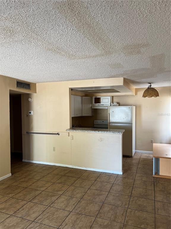 A kitchen with white cabinets and a refrigerator opens to a tiled living area — 800 N FISKE BOULEVARD UNIT 606, COCOA, FL