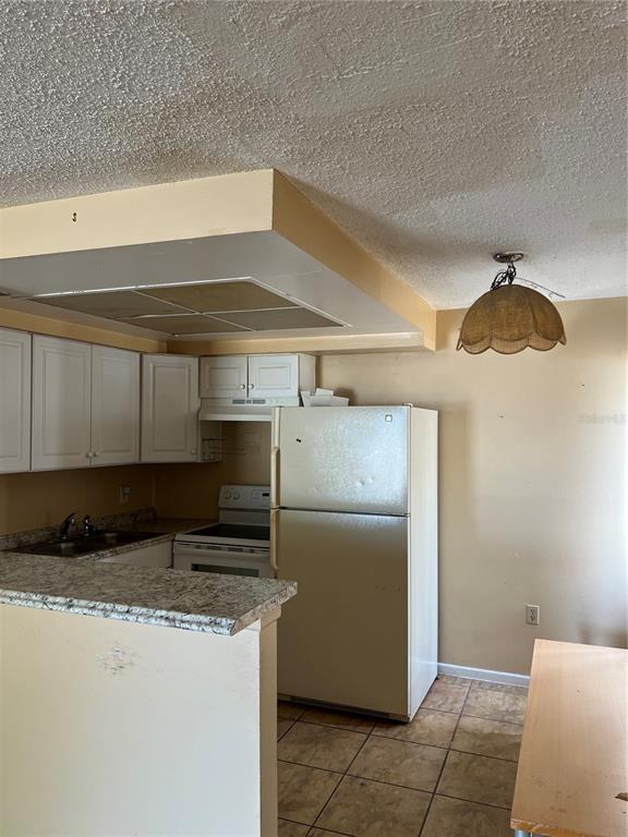 A kitchen features white cabinets, a refrigerator, a stove, and a textured ceiling — 800 N FISKE BOULEVARD UNIT 606, COCOA, FL