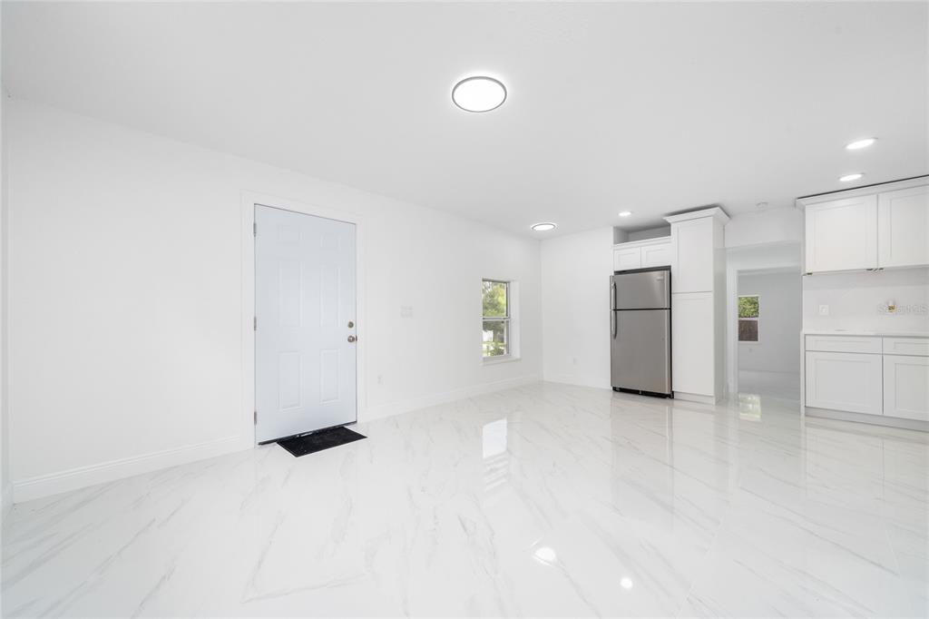 A bright, open-concept kitchen and living area features white cabinetry, stainless appliances, and marble-look flooring — 5621 LUNSFORD DRIVE, ORLANDO, FL